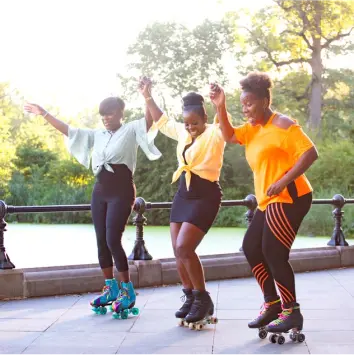 Three happy women holding hands and roller skating at the park