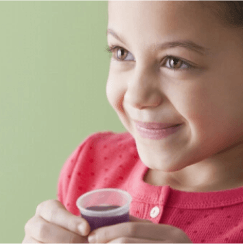Little girl holding dosing cup of purple liquid medicine