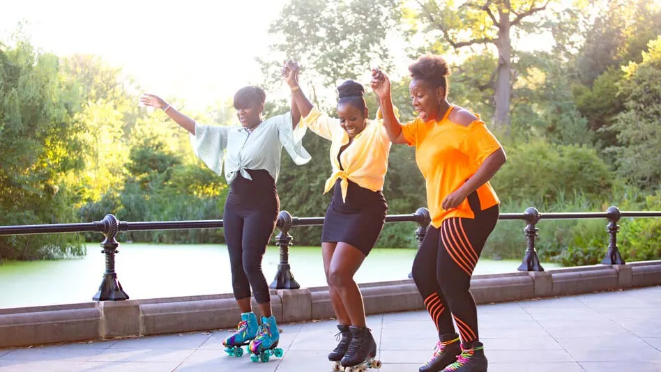 Three happy women holding hands and roller skating at the park