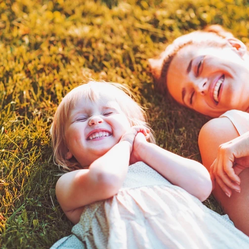 Woman and a little girl smiling, laying down in the grass in the sun