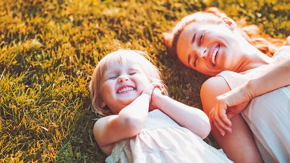 Woman and a little girl smiling, laying down in the grass in the sun